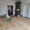 Zabytkowy parkiet w kamienicy przy ul. Śląskiej trakcie renowacji. Na zdjęciu widać bogato zdobiony piec, profesjonalny odkurzacz oraz cykliniarkę.